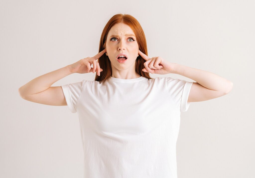 Portrait of stressed young woman covering her ears and gesticulating say no bla-bla-bla standing on white isolated background in studio.