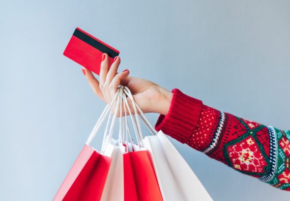 Close up crooped shot of woman hand holding many paper handbags and red credit card