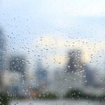 office window covered with rain water. water spray on window. after rain traffic, worker stuck in the office concepts. blur urban skyline background. rainy season concepts.