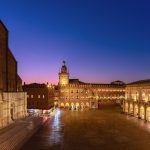Sunset light bathes Piazza Maggiore in Bologna, highlighting the grandeur of its medieval structures against the dusk sky