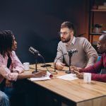 Three radio hosts interviewing a guest in a professional podcast studio, engaging in a discussion and creating audio content