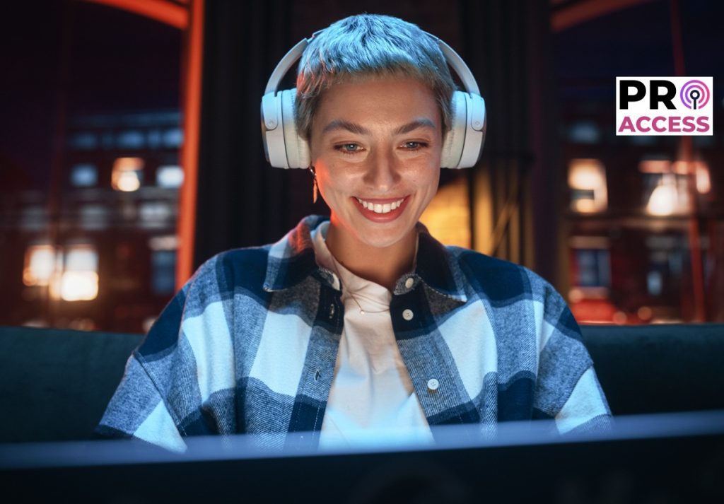 Young Beautiful Woman Wearing Headphones and Working from Home on Laptop Computer in Cozy Stylish Loft Apartment. Creative Female Smiling, Checking Social Media, Browsing Internet.